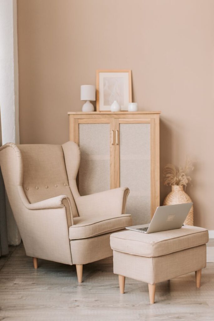 Beige armchair and footstool with laptop in a minimalist living room setting.